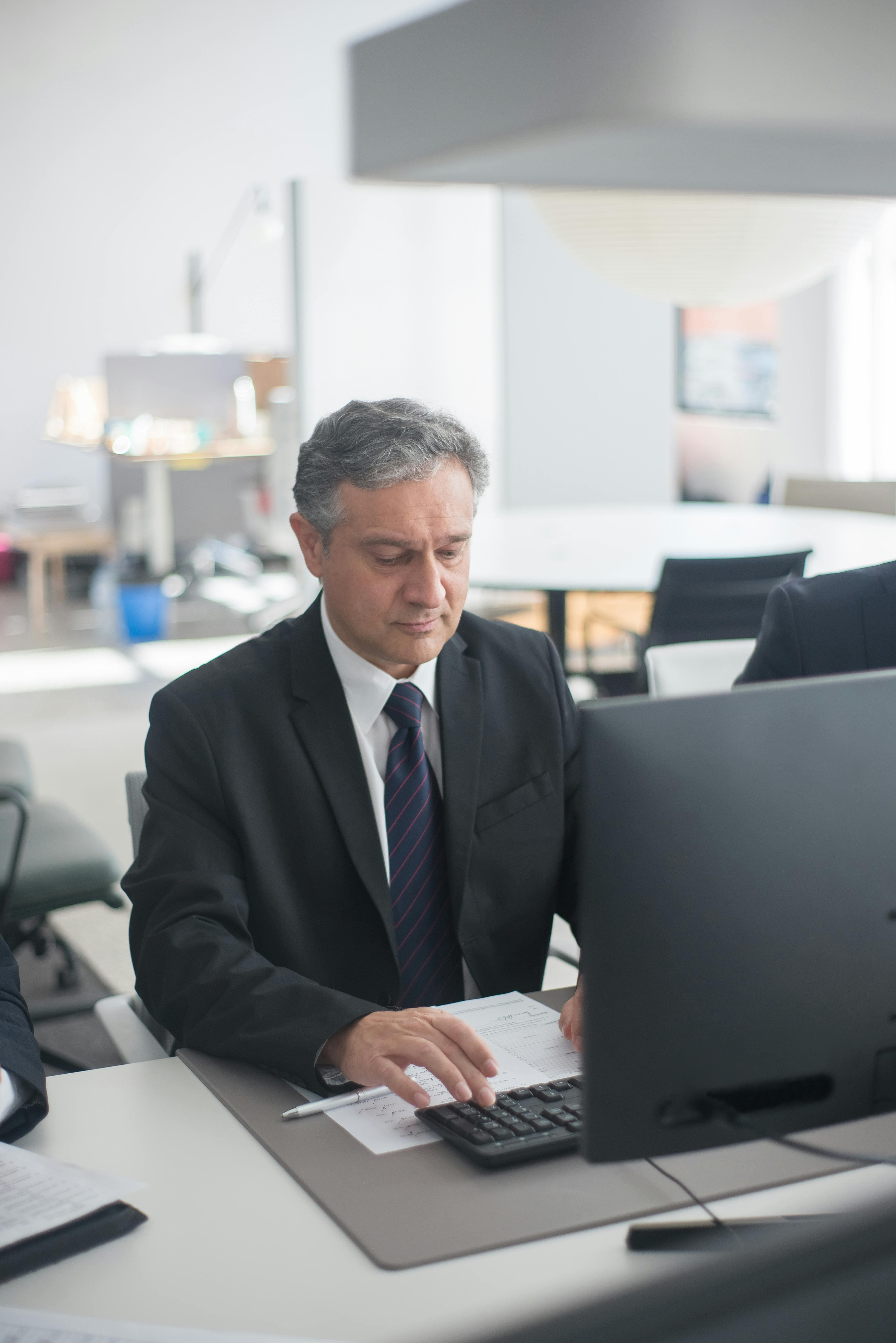 Directivo con traje revisando documentación frente al monitor en su oficina, imagen del responsable empresarial que asume las sanciones LISOS y los recargos de prestaciones cuando la empresa no evalúa riesgos psicosociales