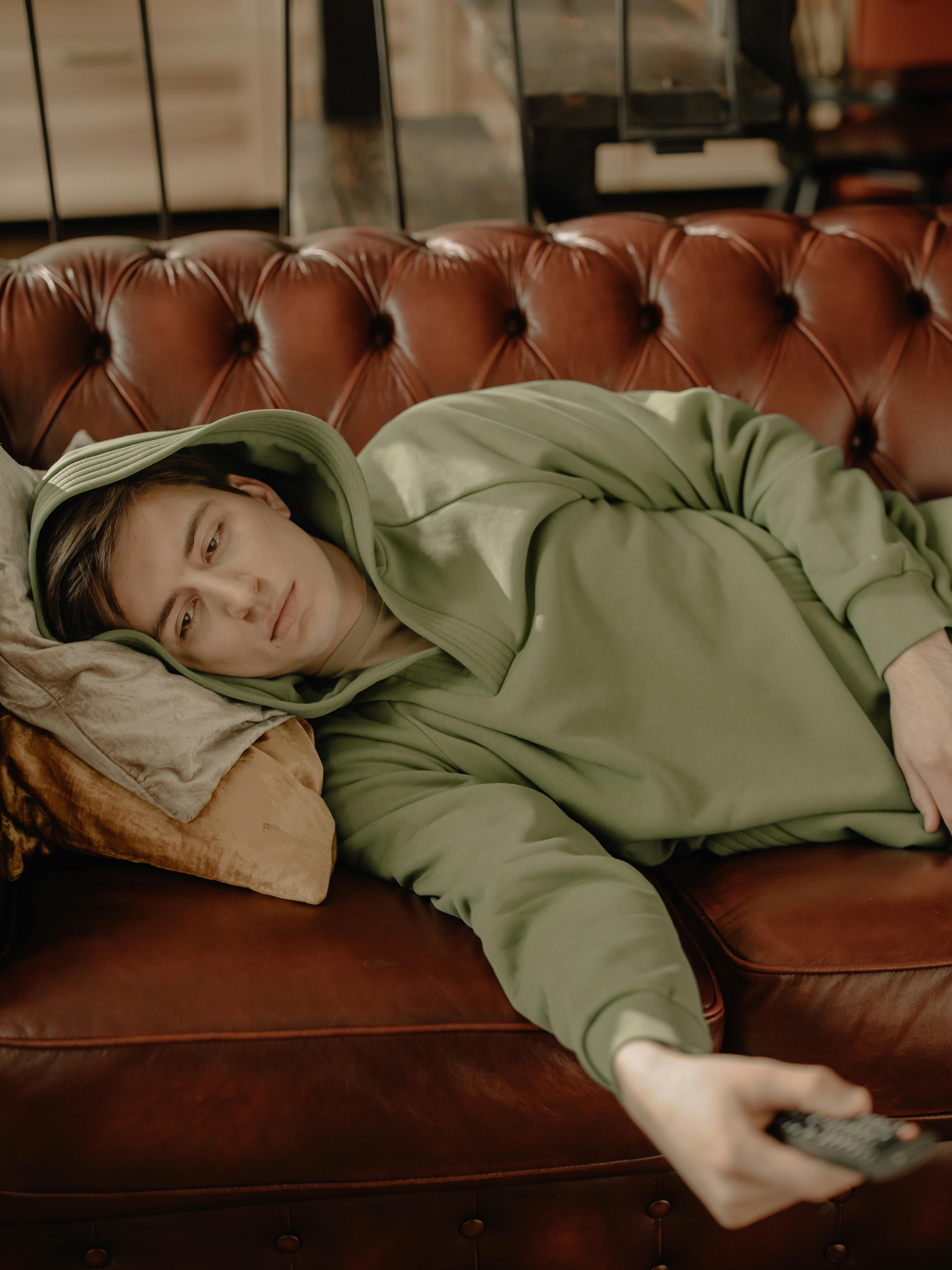 Person lying on a sofa with the TV remote, image of the prolonged sedentarism that often goes hand in hand with anxiety and depressive symptoms